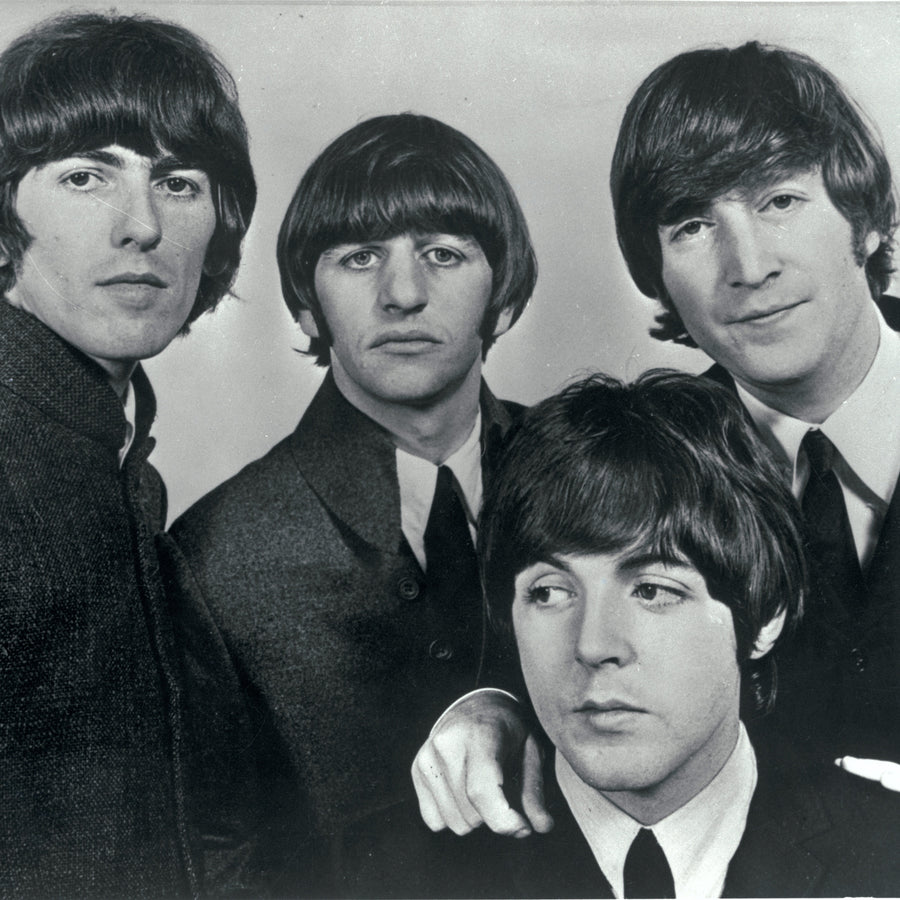 Black and white portrait photograph of The Beatles, likely a band or group, standing together against a plain studio background.