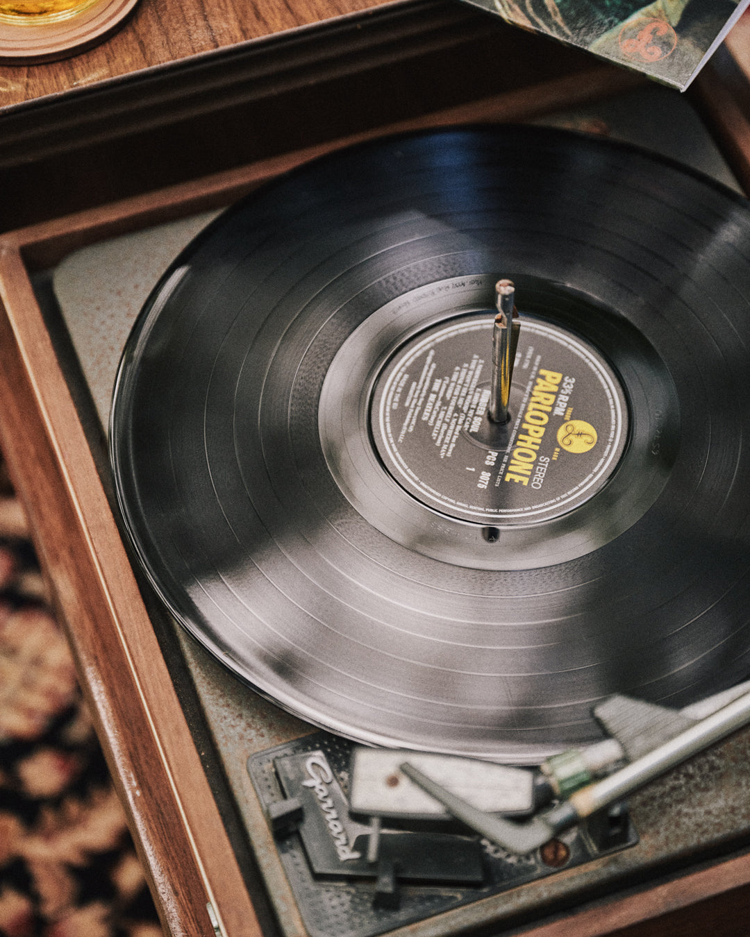 A close-up of a vintage wooden record player with a black vinyl record spinning inside, showing the center label and part of the tonearm.